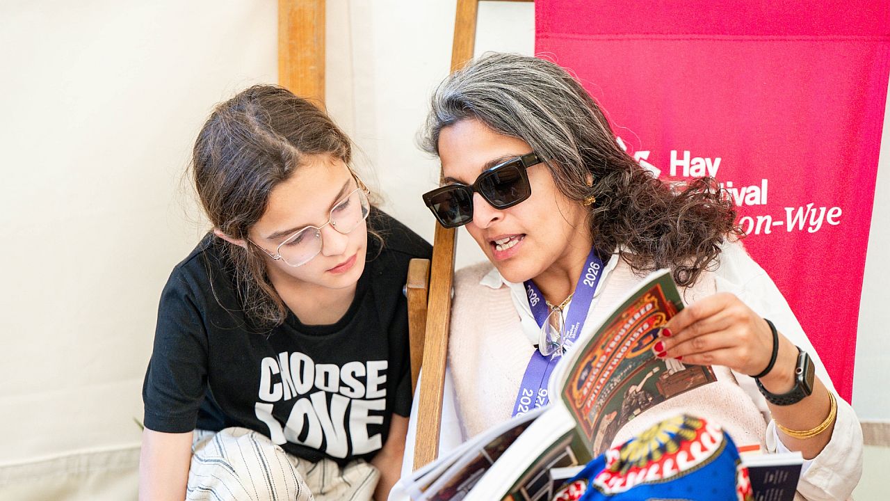 A mother and child reading a book in the Hay Festival gardens
