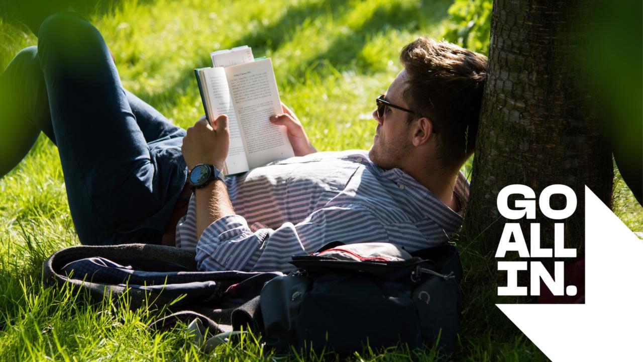 A man reading a book sat underneath a tree