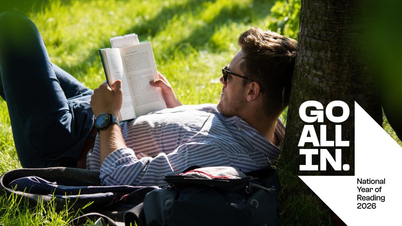 A man reading a book sat underneath a tree